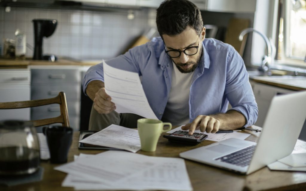 Home Business Insurance, photo of man working from home with laptop, calculator and papers