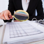 Paying too much for an audit, business person looking at file with magnifying glass